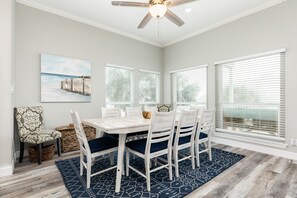 Un coin repas avec une table blanche, des chaises bleues et un ventilateur de plafond.