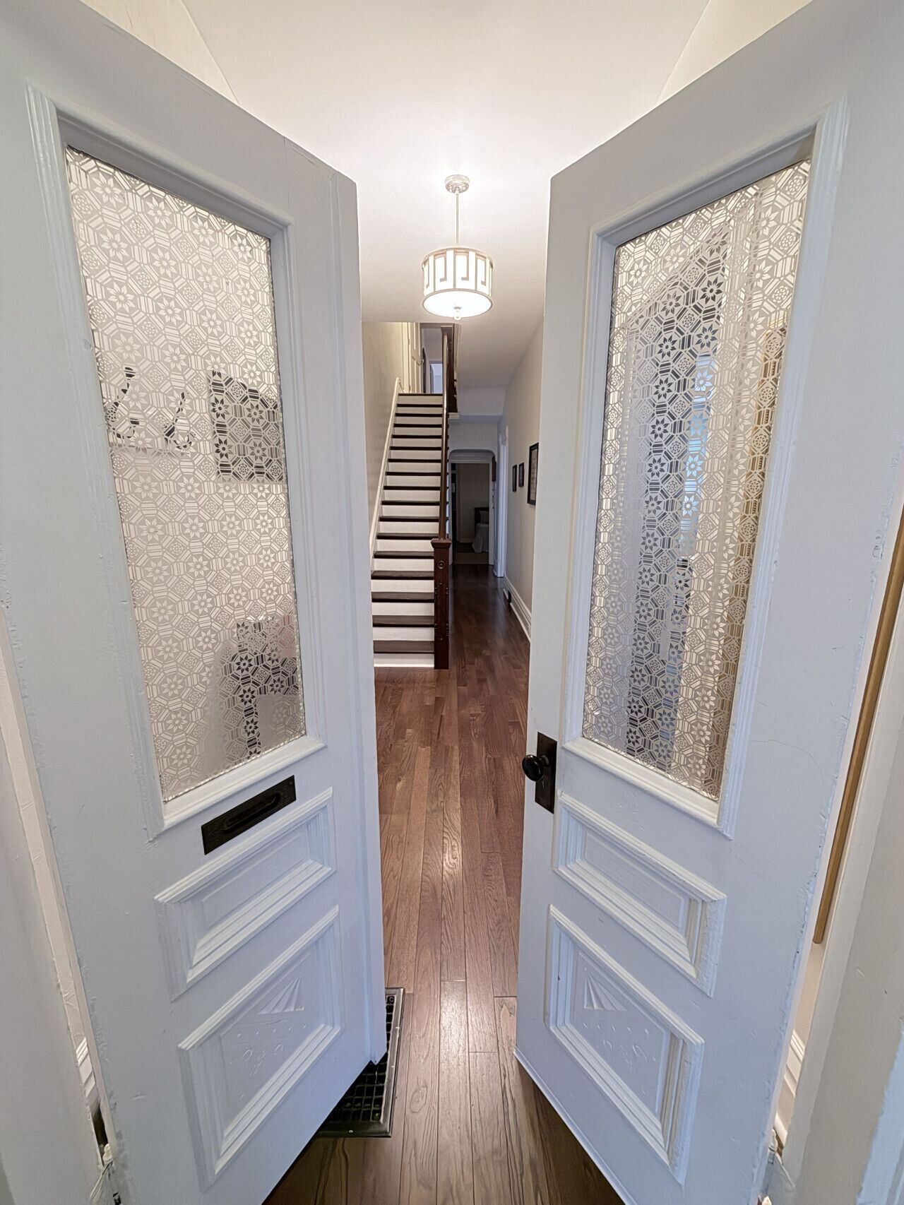 Un couloir doté de portes en verre à motifs, d’un plancher en bois et d’un escalier menant à un autre niveau.