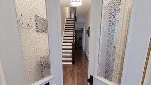 Un pasillo con puertas de vidrio con diseños, piso de madera y una escalera que sube a otro nivel.
