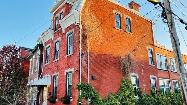 Un edificio de ladrillo rojo con detalles blancos, varias ventanas y un porche con escalones.