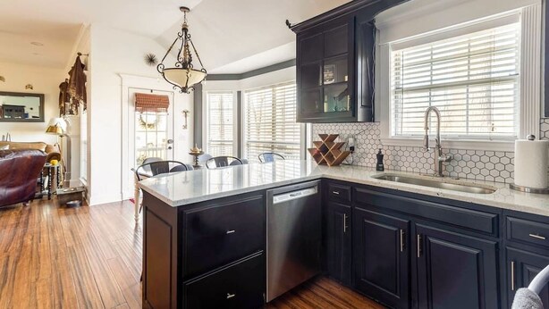 A modern kitchen with dark cabinetry, a central island, and a large window with blinds. - Pool + Hot Tub + Theater · Countryside Retreat (Hermitage)