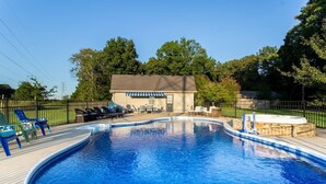 A swimming pool with lounge chairs and a hot tub, surrounded by a wooden deck and a fenced area. - Pool + Hot Tub + Theater · Countryside Retreat (Hermitage)