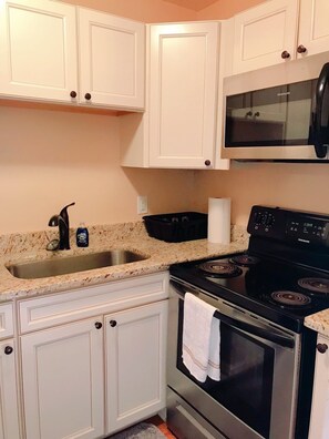 A kitchen with white cabinets, a stainless steel sink, a black stove, and a microwave above the stove.