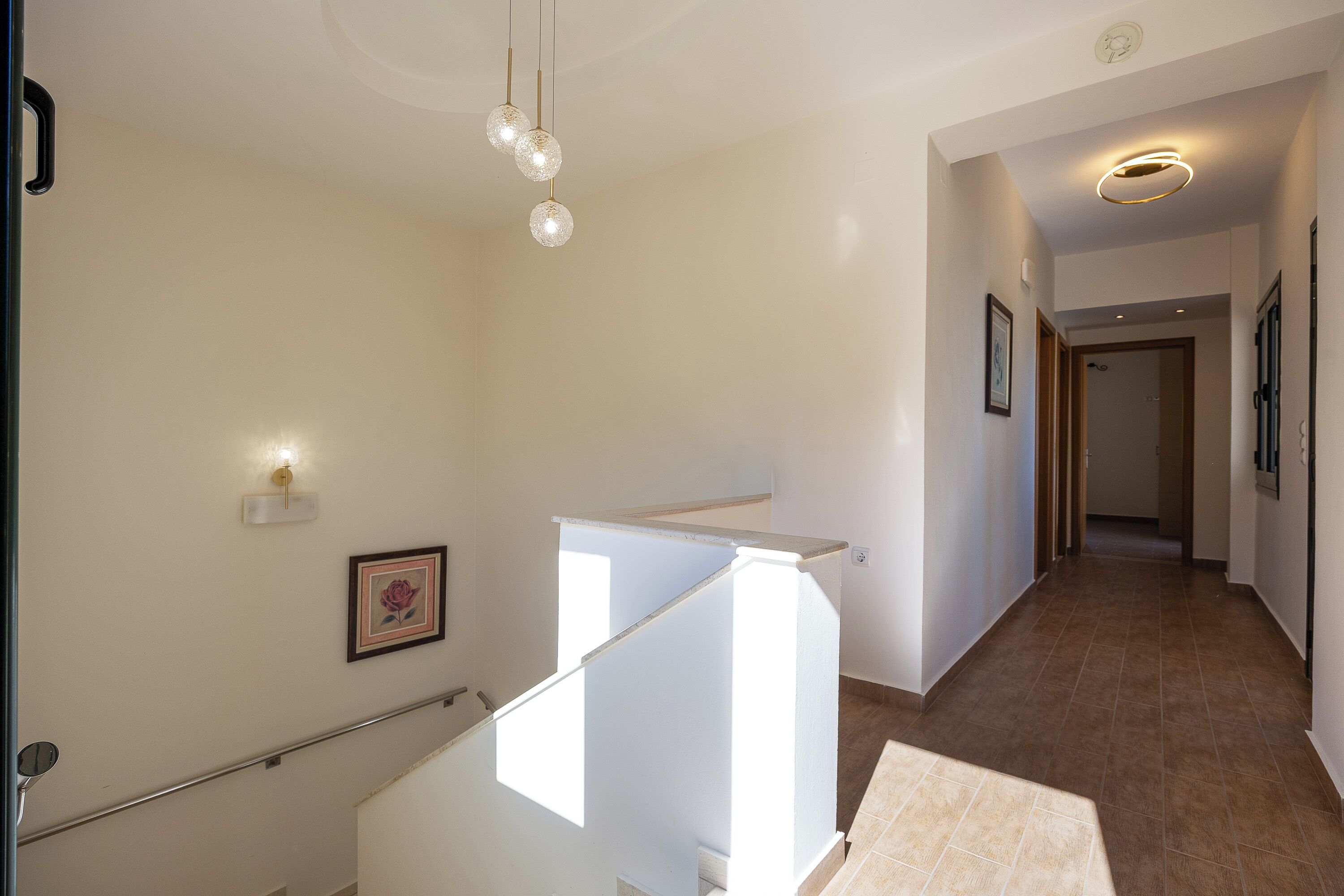 A hallway with a staircase, a light fixture, and a framed picture on the wall.