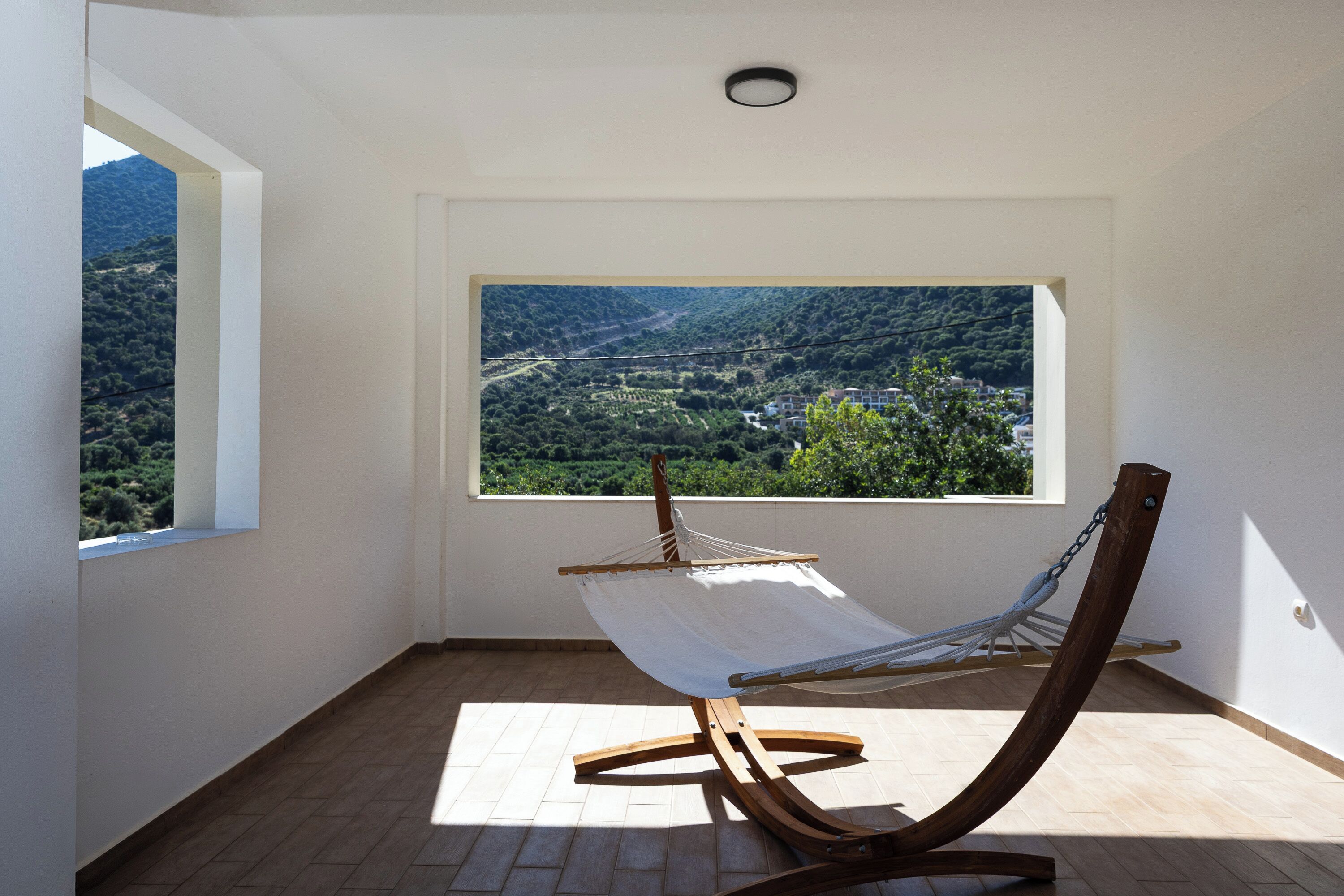 Een hangmat in een kamer met een groot raam, een betegelde vloer en uitzicht op een bergachtig landschap.