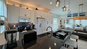 A modern kitchen with white cabinets, a black countertop, and a central island. There are hanging pendant lights and a microwave above the stove. - Manatee Haven: Screened Pool, Spa, Elevator (Captiva)