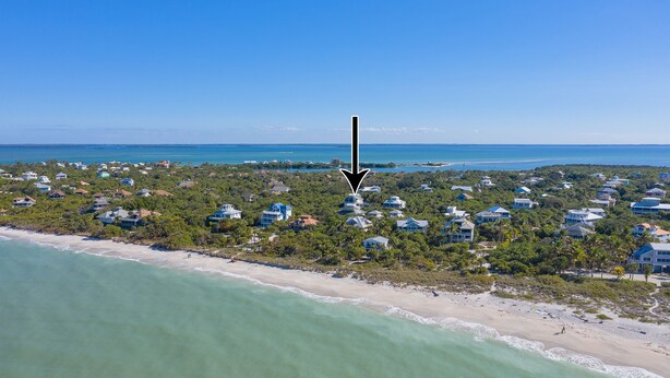 An aerial view of a coastal area with houses along the beach, a clear blue sky, and a calm sea. - Manatee Haven: Screened Pool, Spa, Elevator (Captiva)
