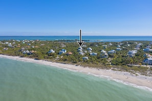An aerial view of a coastal area with houses along the beach, a clear blue sky, and a calm sea.