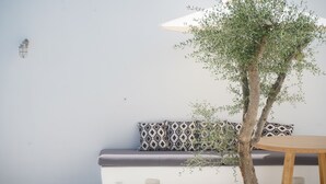 A minimalist room with a wooden table, a bench with patterned cushions, and a tree. - Alio Suites-Suite N2 with private swimming pool (Νάξος)