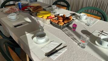 Een ontbijttafel gedekt met borden, bestek, een mand met croissants en een schaal fruit.