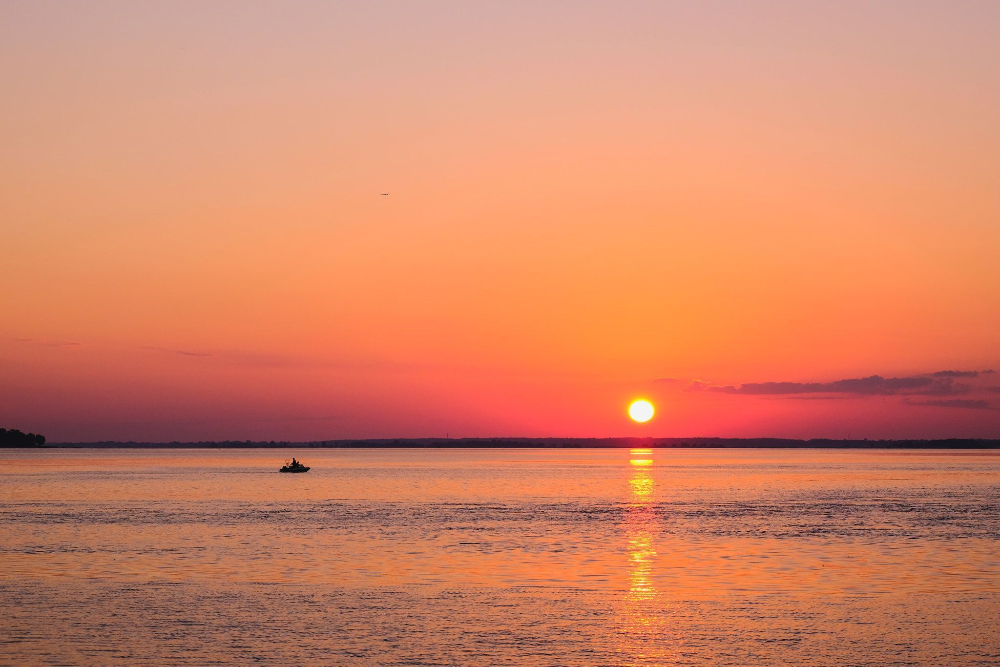 A sunset over a calm body of water with a boat in the distance.