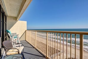 A balcony with a view of the beach, featuring a chair and a table.