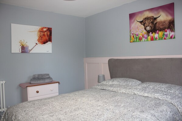 A bedroom with a bed, a nightstand, a radiator, and two wall art pieces. - 1-bed Apartment in Wells (Wells)