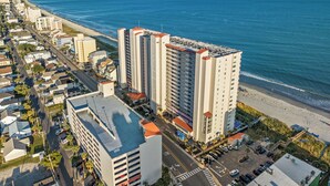 Un hotel costero con varios edificios altos, una playa y un estacionamiento.