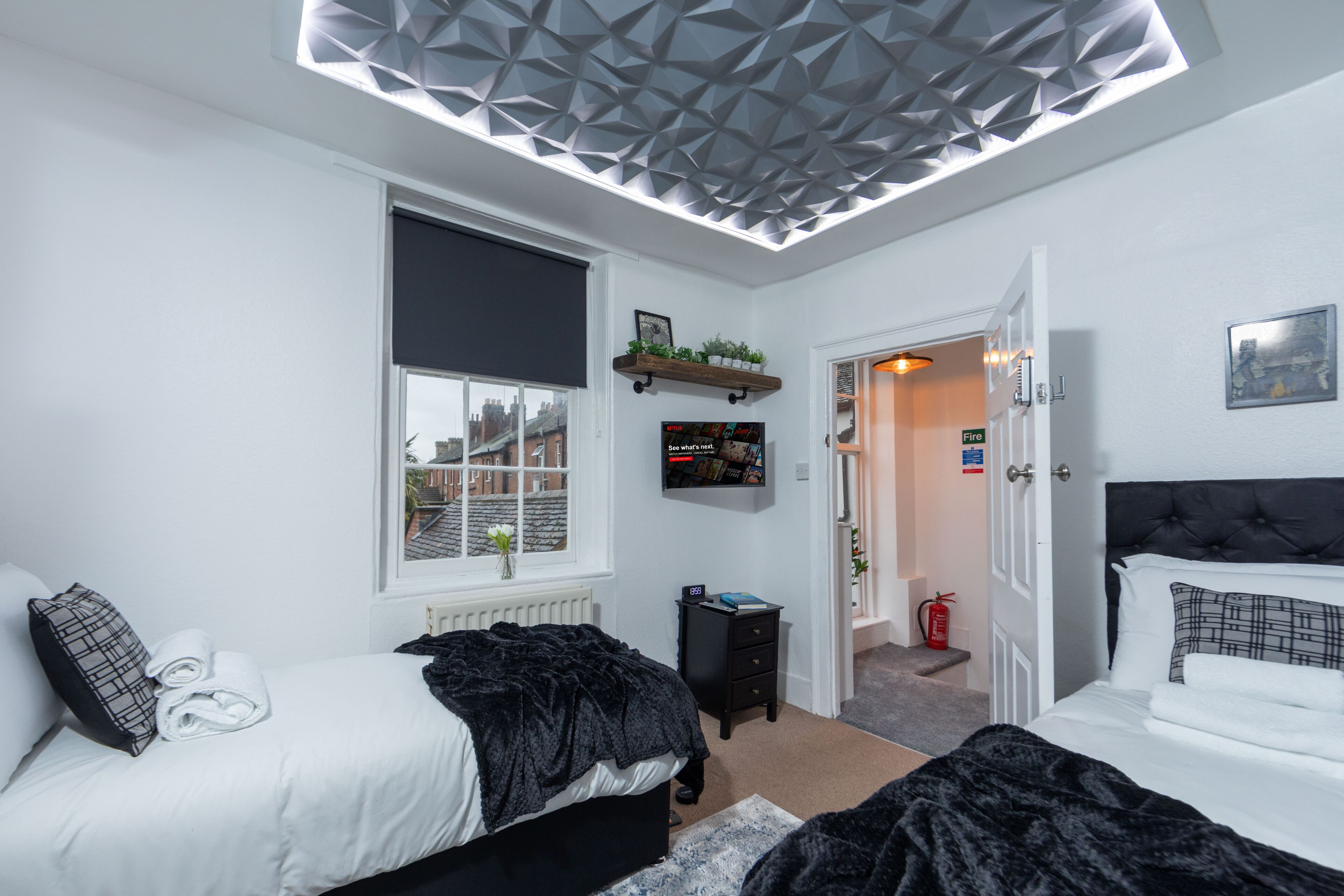 Una camera da letto moderna con due letti, un'ampia finestra vista panoramica, una TV a parete e un originale design geometrico del soffitto.