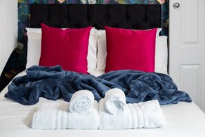 A neatly made bed with white and pink pillows, a blue blanket, and rolled white towels. - 6 Bedroom City Centre Townhouse (Canterbury)