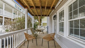 Une terrasse en bois avec deux fauteuils en osier et une table, des rampes blanches et un espace couvert doté d’un plafond en bois.