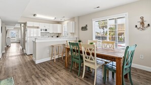 Une cuisine moderne avec des meubles blancs, un îlot central et un coin repas comprenant des chaises et une table en bois.