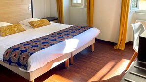 Habitación de hotel con cama, suelo de madera y ventana con cortinas amarillas.