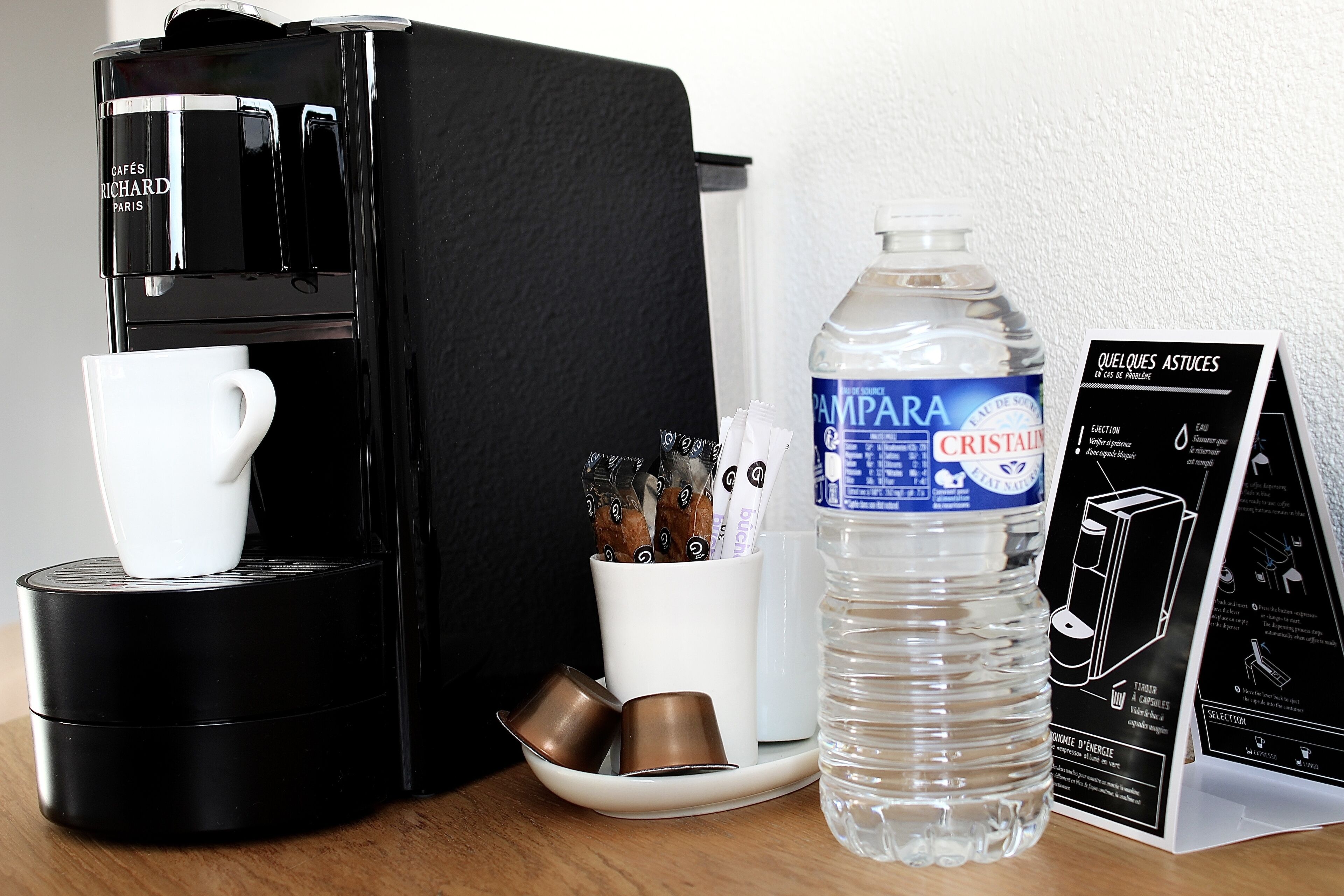 Eine Kaffeemaschine, eine Wasserflasche, eine Tasse und ein Kaffee-Pod-Halter auf einer Tischplatte.