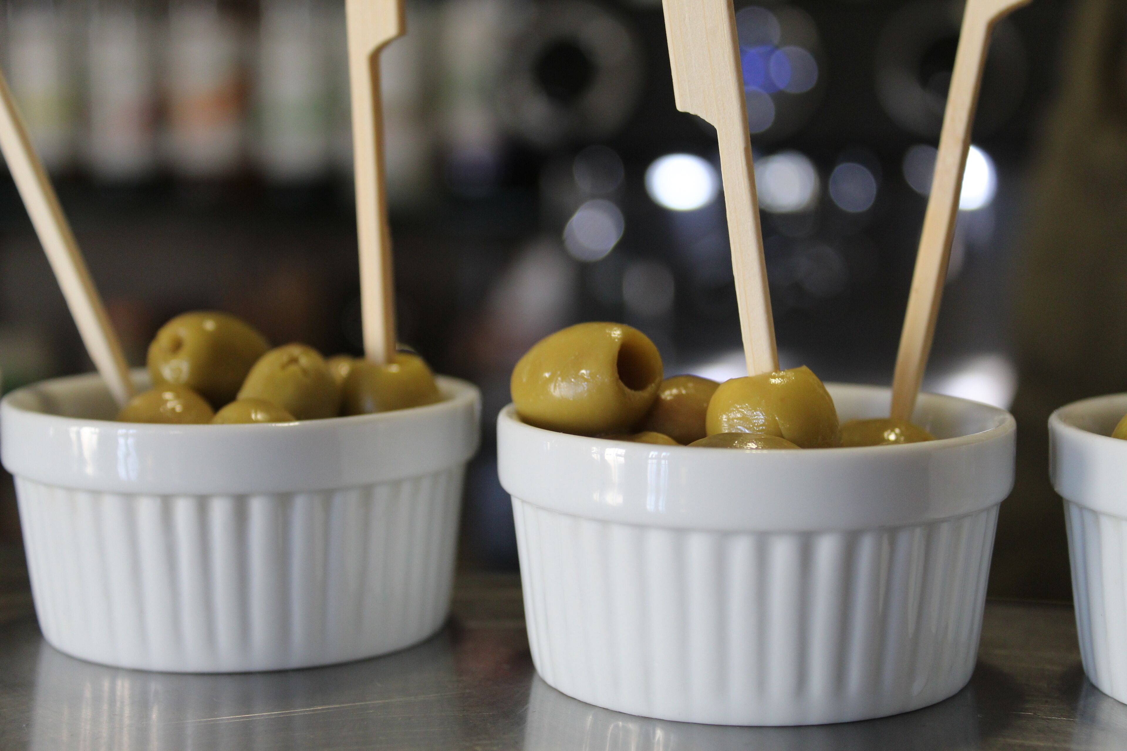 Tres recipientes blancos con aceitunas y palitos de madera.