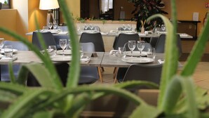 Un restaurante con mesas dispuestas para comer, sillas y una planta al fondo.