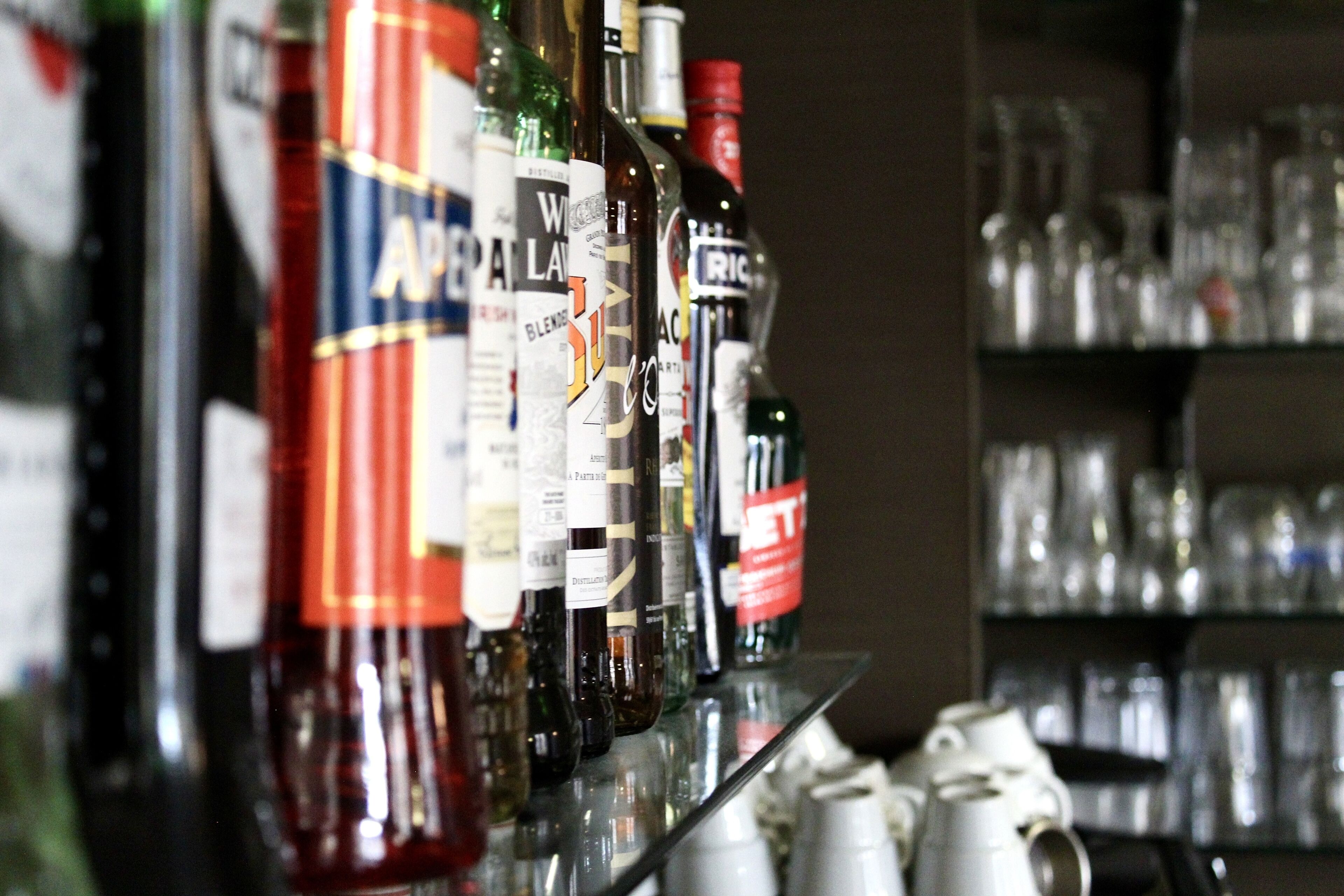 A row of liquor bottles on a shelf with glasses behind them.
