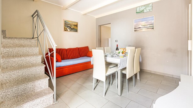 A modern living space with a staircase, a red sofa, a dining area with a table and chairs, and artwork on the walls. - Casa Conchiglia by BarbarHouse (Gallipoli)