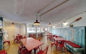 L’intérieur d’un restaurant avec des tables et des chaises rouges, un banc en bois et un mur sur lequel est écrit le mot « PLAGE ».