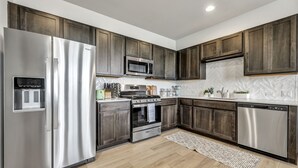 A modern kitchen with stainless steel appliances, dark wooden cabinets, and a herringbone tile backsplash. - Cozy Secluded Studio With Full-Kitchen, Washer And Dryer - The Works! (Austin)