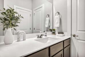 A modern bathroom with a white sink, two towel racks, a mirror, and a potted plant. - Cozy Secluded Studio With Full-Kitchen, Washer And Dryer - The Works! (Austin)