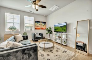 A modern living room with a sofa, a coffee table, a TV, and artwork on the wall. - Cozy Secluded Studio With Full-Kitchen, Washer And Dryer - The Works! (Austin)