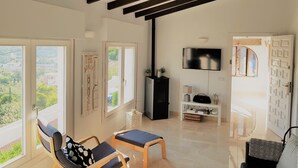 Amplia sala de estar con techo alto, ventanas grandes que ofrecen vistas al exterior, un televisor de pantalla plana montado en la pared y una consola blanca con diversos objetos.