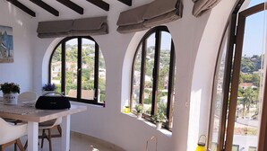 Una habitación con techo curvo, amplias ventanas arqueadas, una mesa de comedor y un pequeño armario blanco.