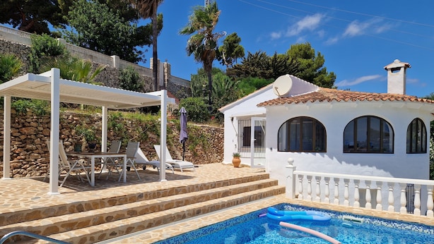Un área de piscina con solárium empedrado, sillones de descanso y una zona de estar cubierta.