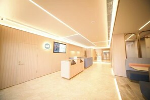 A modern hotel lobby with a reception desk, a seating area, and a staircase leading to another level. - HanTing Hotel (Beijing Xidan Mall) (Beijing)