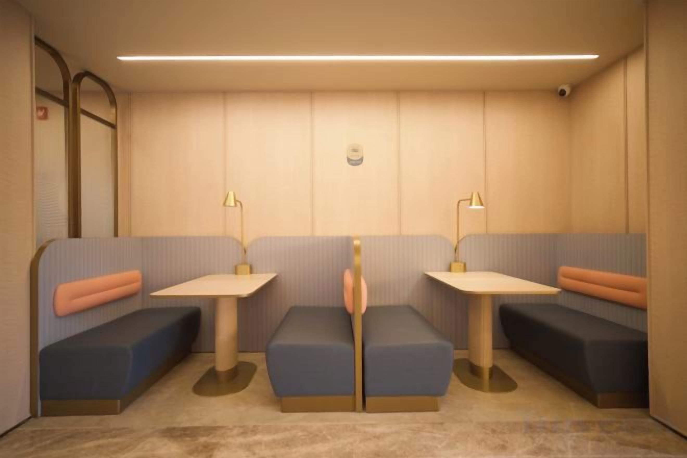 A room with two seating areas, each with a table and lamp, and a wall-mounted camera.