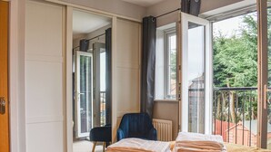 Ein Schlafzimmer mit einem Bett, einem Sessel und Blick auf einen Balkon mit Geländer.