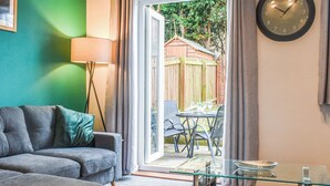 Ein Wohnzimmer mit grauem Sofa, einem Glastisch, einer Lampe und einer Wanduhr.