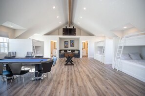 A spacious loft-style room with a pool table, a sofa, and bunk beds.
