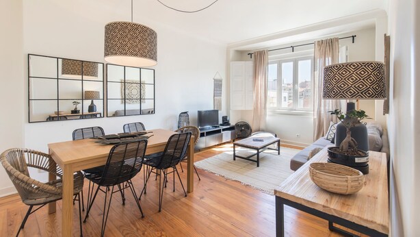 Una sala moderna con una mesa de comedor de madera, sillas negras, un televisor y un ventanal con cortinas.