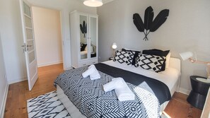 A neatly made bed with patterned bedding, a bedside lamp, and a wall-mounted feather decoration.