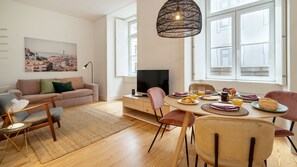 Un salon moderne comprenant un canapé, un téléviseur, une table à manger avec des chaises et une grande fenêtre donnant sur un paysage urbain.