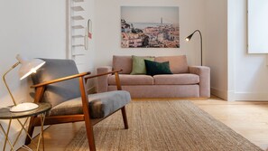A living room with a modern chair, a sofa, a lamp, and a painting of a cityscape.