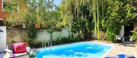 Relax by the pool surrounded by lush greenery and a weeping willow tree.