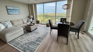 A spacious living room with a large window, a ceiling fan, a dining area with chairs, a sofa, and a coffee table.