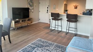 A living room with a TV, a coffee bar, and two bar stools.
