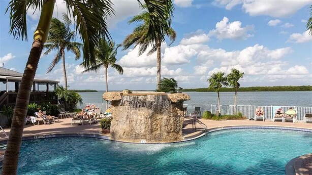 A pool with a waterfall feature surrounded by palm trees and lounge chairs.