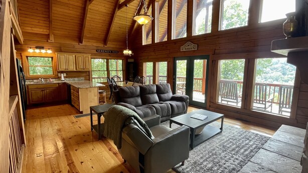 A cabin interior with a kitchen, dining area, and a living room with a sofa and a table. - Beautiful secluded cabin - sleeps 12, fire pit, fishing pond, grill, game room (russell springs)