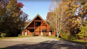 A log cabin with a front porch, surrounded by trees with autumn foliage. - Beautiful secluded cabin - sleeps 12, fire pit, fishing pond, grill, game room (russell springs)